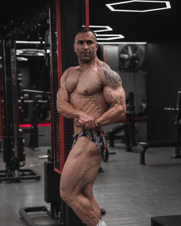 Bodybuilder showcasing physique in modern gym setting, flexing muscles.