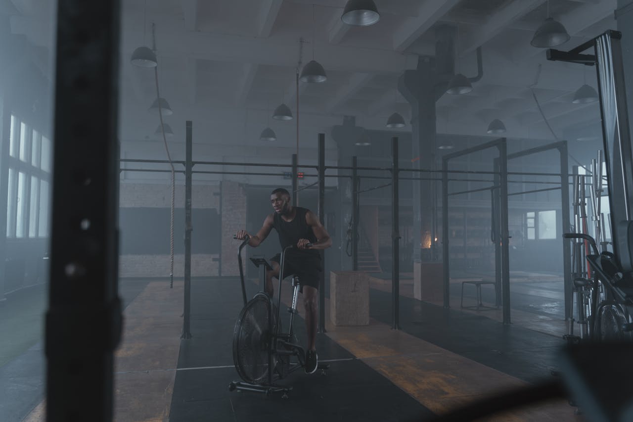 Focused athlete exercising in an industrial-style gym on a stationary bike for fitness and strength.